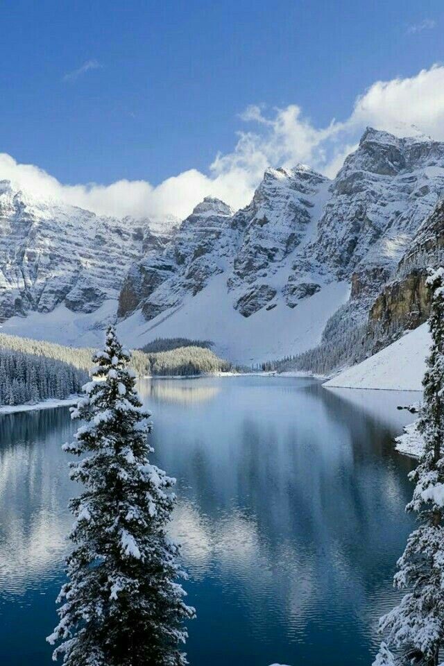 the snow covered mountains are reflected in the still waters of this mountain lake, which is surrounded by pine trees and evergreens