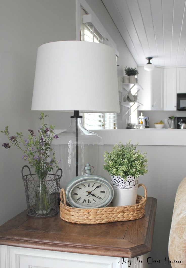 a table with a lamp, clock and potted plants sitting on top of it