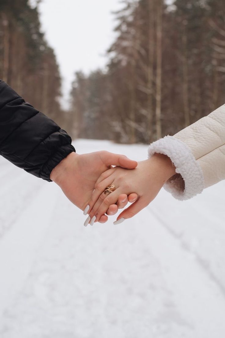 two people holding hands while walking in the snow