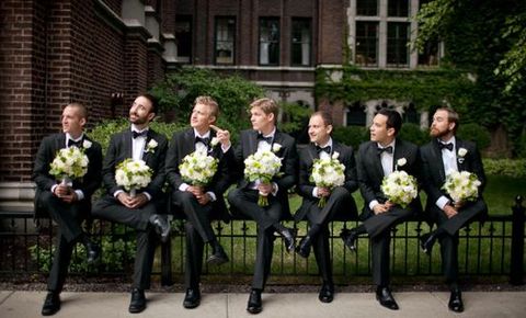 a group of men in tuxedos are sitting on a bench with bouquets