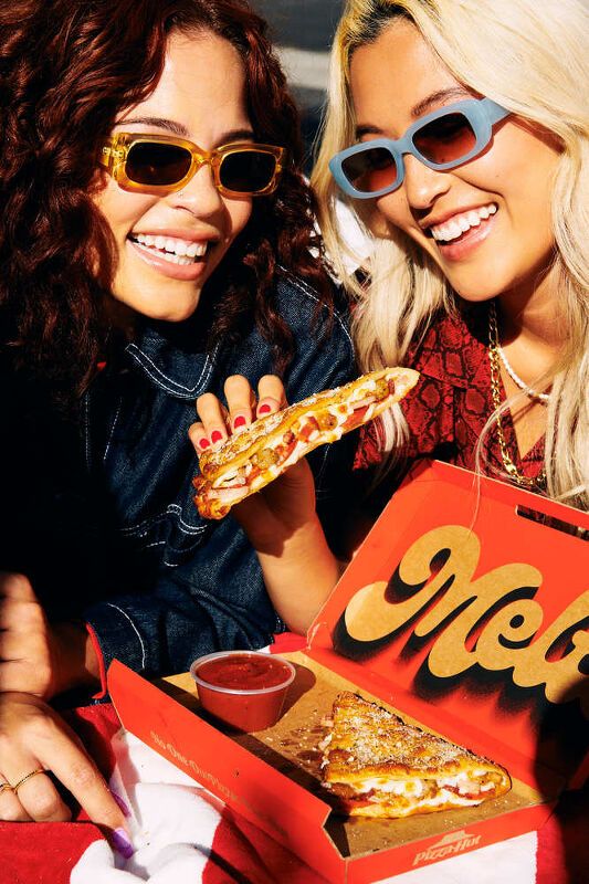 two beautiful young women sitting next to each other holding slices of pizza in their hands