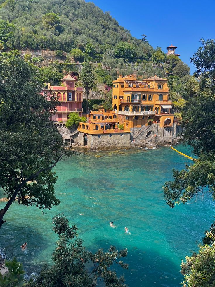 people swimming in the clear blue water near an orange building on top of a hill