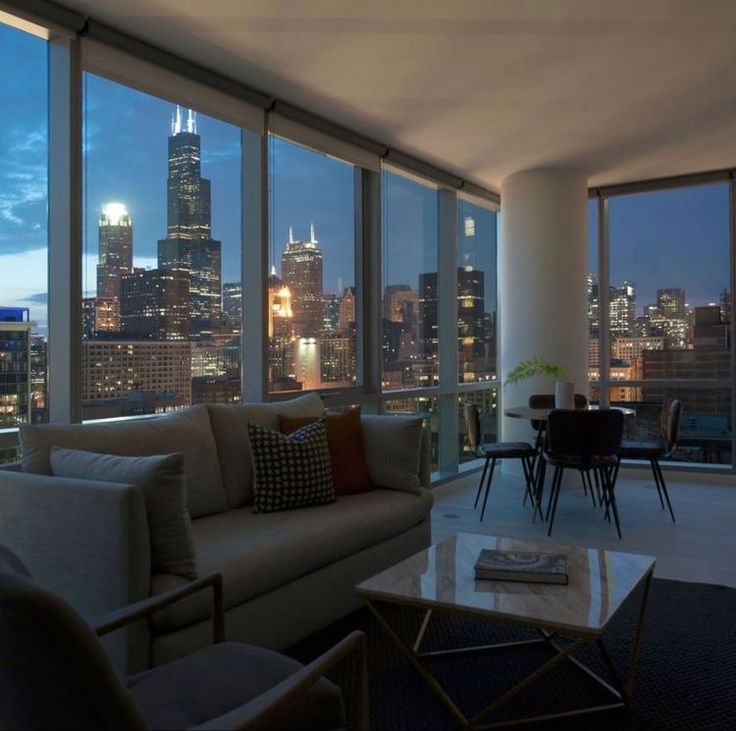 a living room filled with furniture and large windows overlooking the city skyline at night time