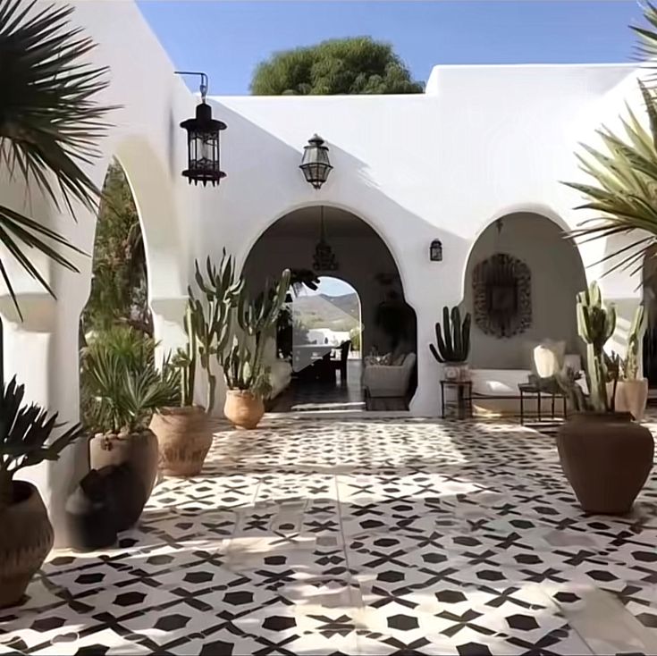 an outdoor patio with potted plants and chairs on the floor, in front of a white building