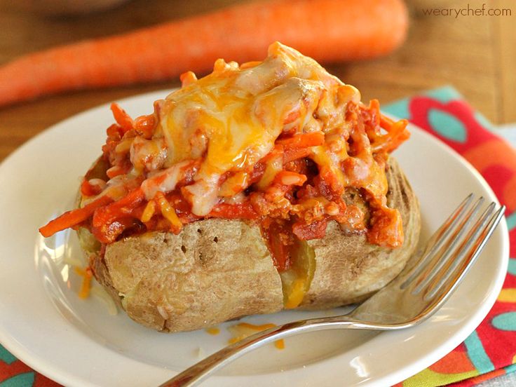 a white plate topped with a baked potato covered in chili and cheese next to carrots