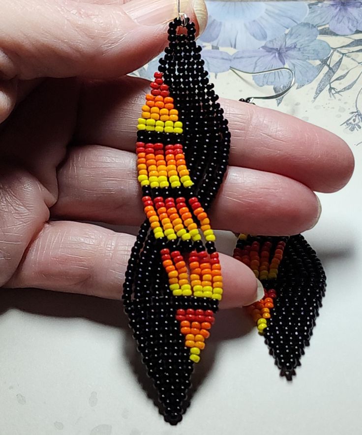 a hand holding a pair of earrings made out of beaded corn on the cob