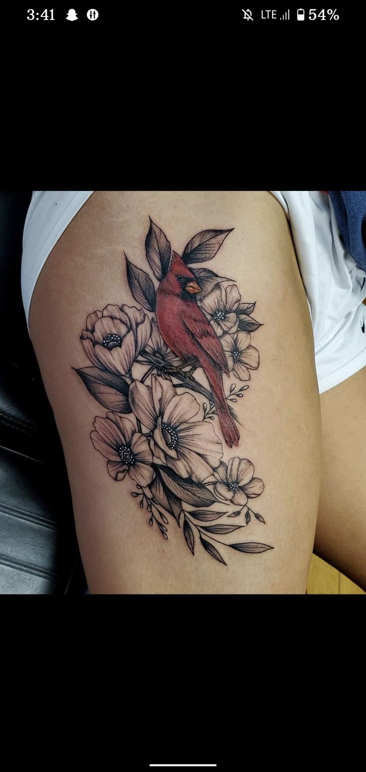 a woman's thigh with flowers and a cardinal tattoo on the side of her leg