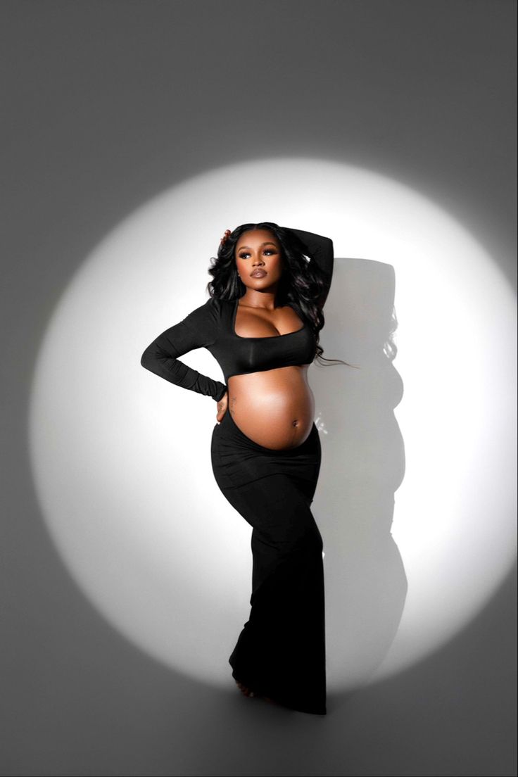 a pregnant woman posing for the camera in a black dress with her hands on her hips