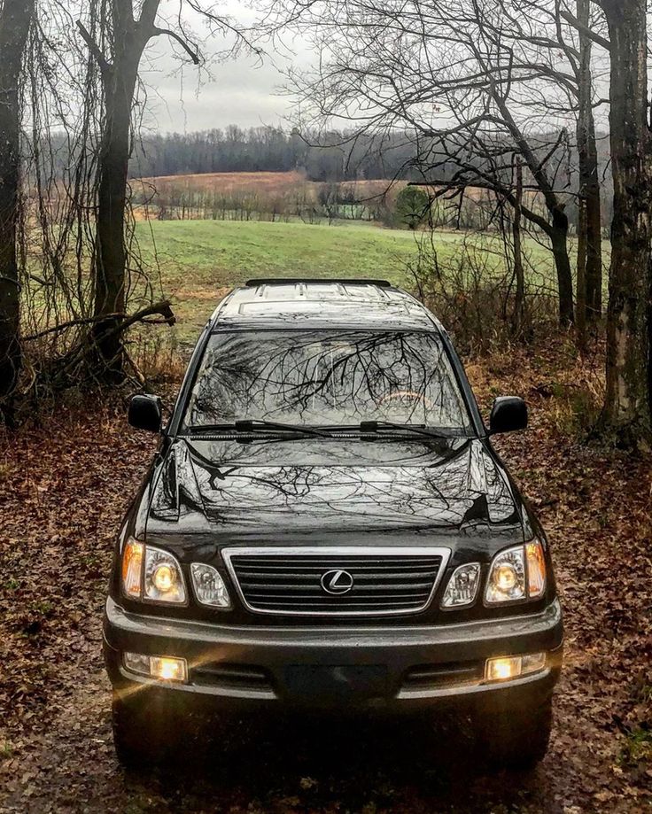 a black car parked in the middle of a wooded area with trees and grass behind it