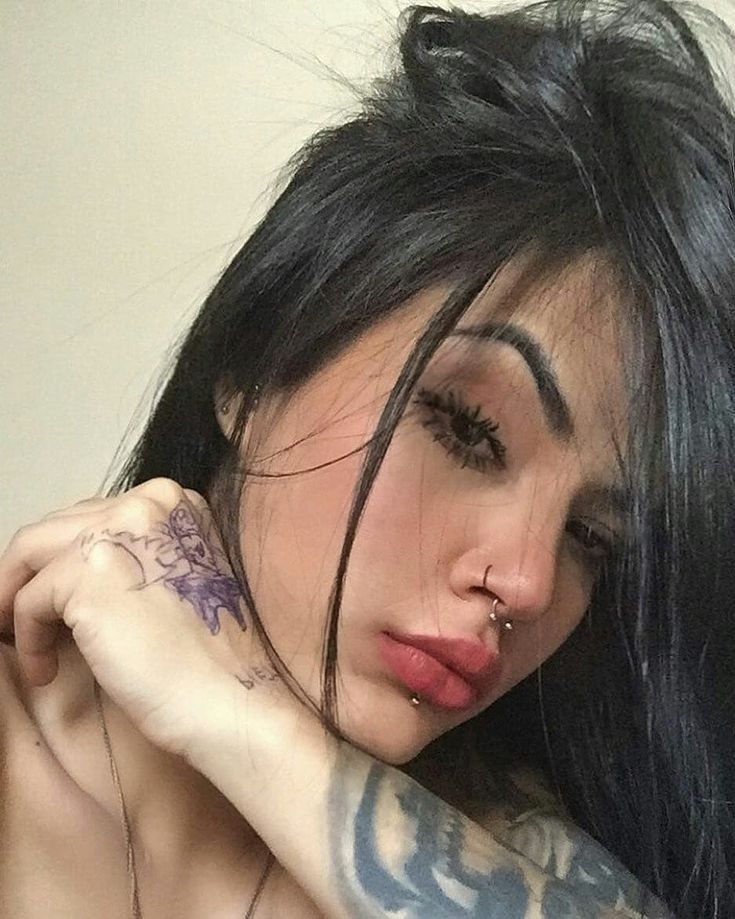 a woman with long black hair and tattoos on her arm is looking at the camera