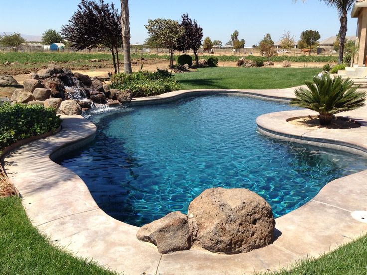 a small pool with rocks and water features landscaping around the perimeter, including palm trees