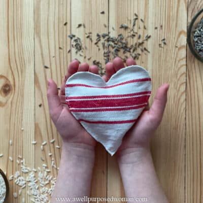 two hands holding a heart shaped bag with seeds in it on top of a wooden table