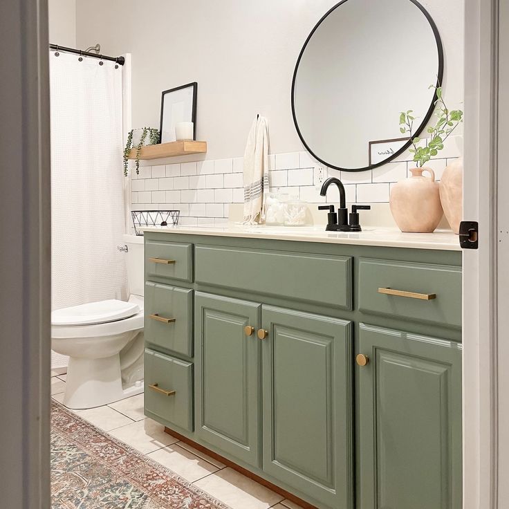 a bathroom with green cabinets and a round mirror on the wall above the sink, along with a rug