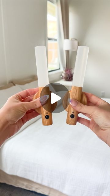 two hands holding wooden objects in front of a bed