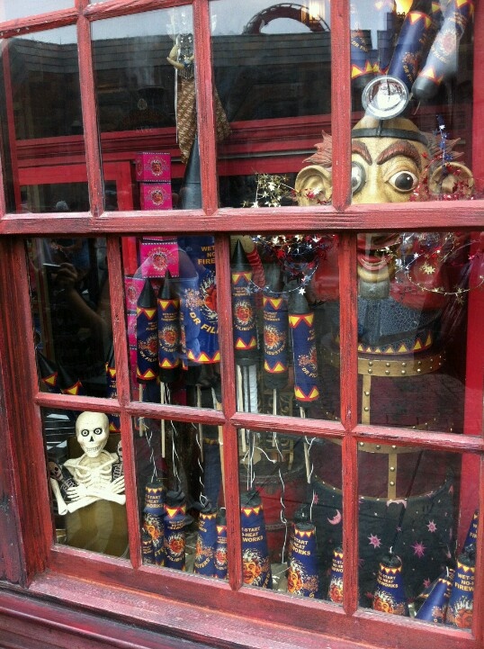 a window with many items in it and a skeleton on the other side, behind which is a red frame