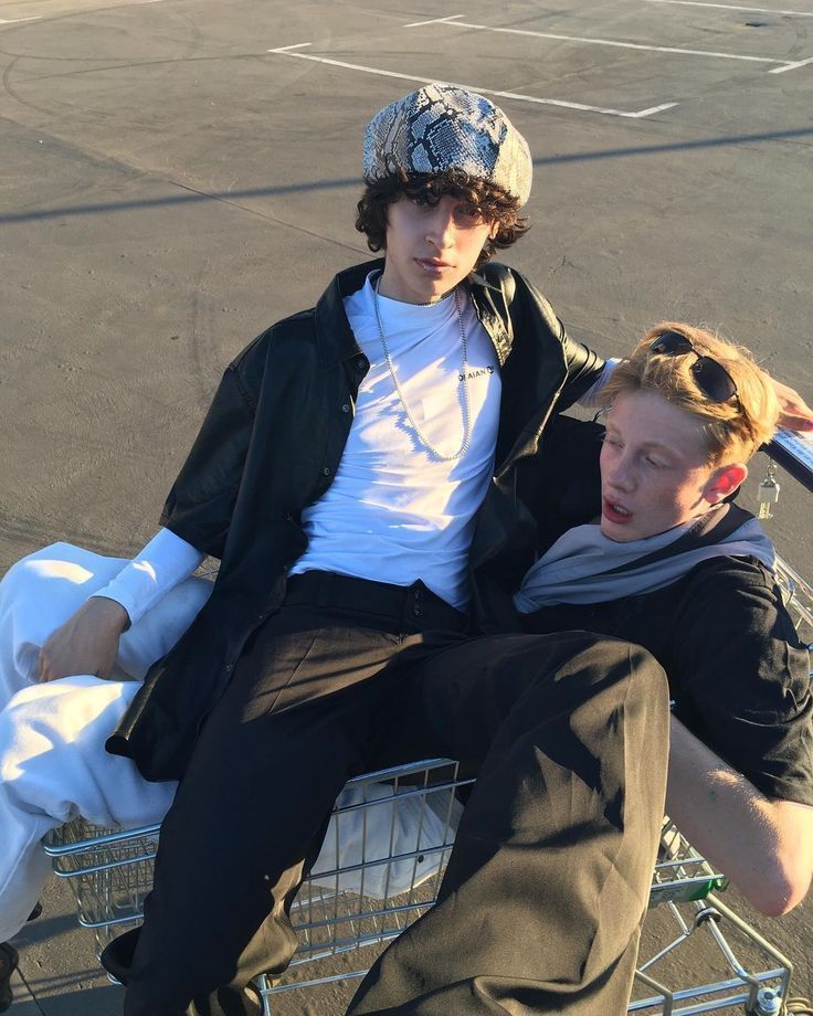 two young men sitting on top of a shopping cart