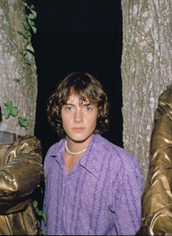 two young men standing next to each other in front of a tree with leaves on it