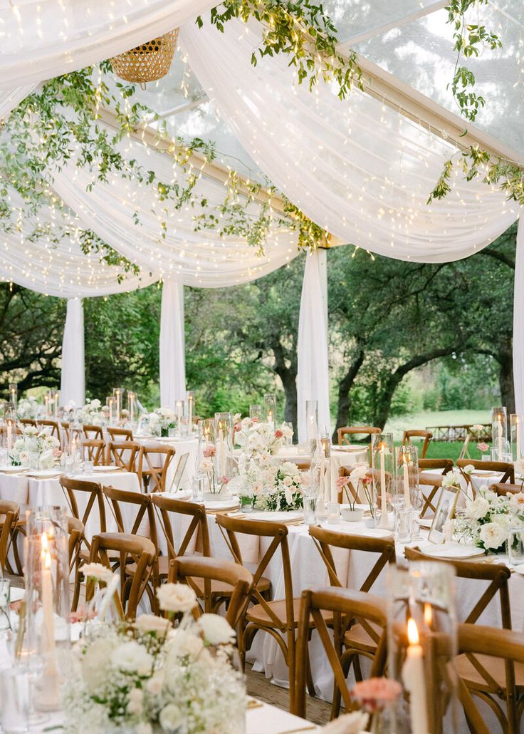 the tables are set up with white flowers and greenery for an outdoor wedding reception