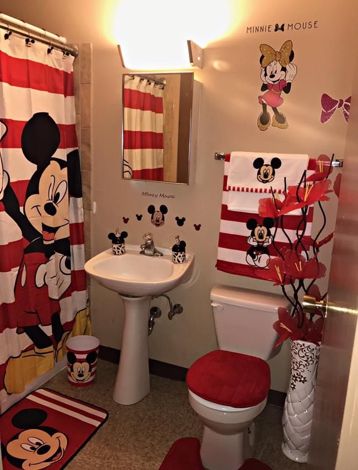 a bathroom decorated in red and white with mickey mouse decorations on the walls, toilet, sink, and shower curtain