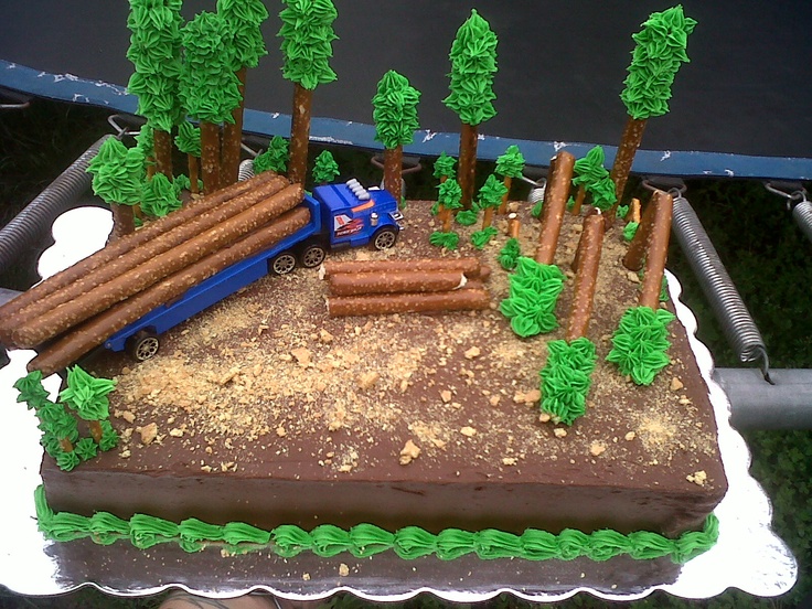 a birthday cake decorated with trees, logs and a truck on the road in front of it