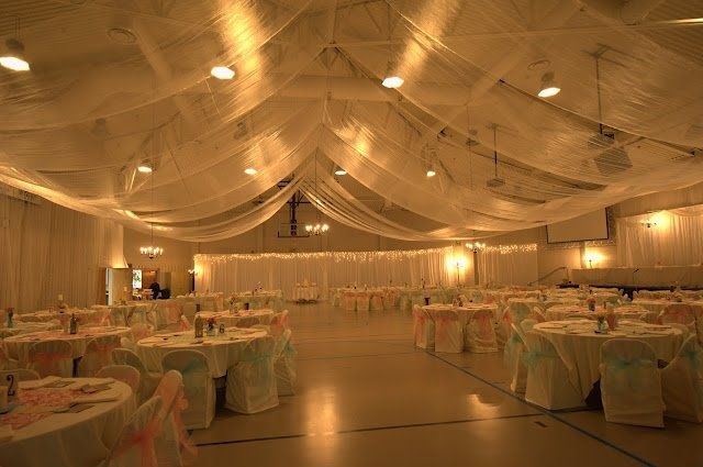 a banquet hall with tables and chairs covered in white draping, decorated with lights