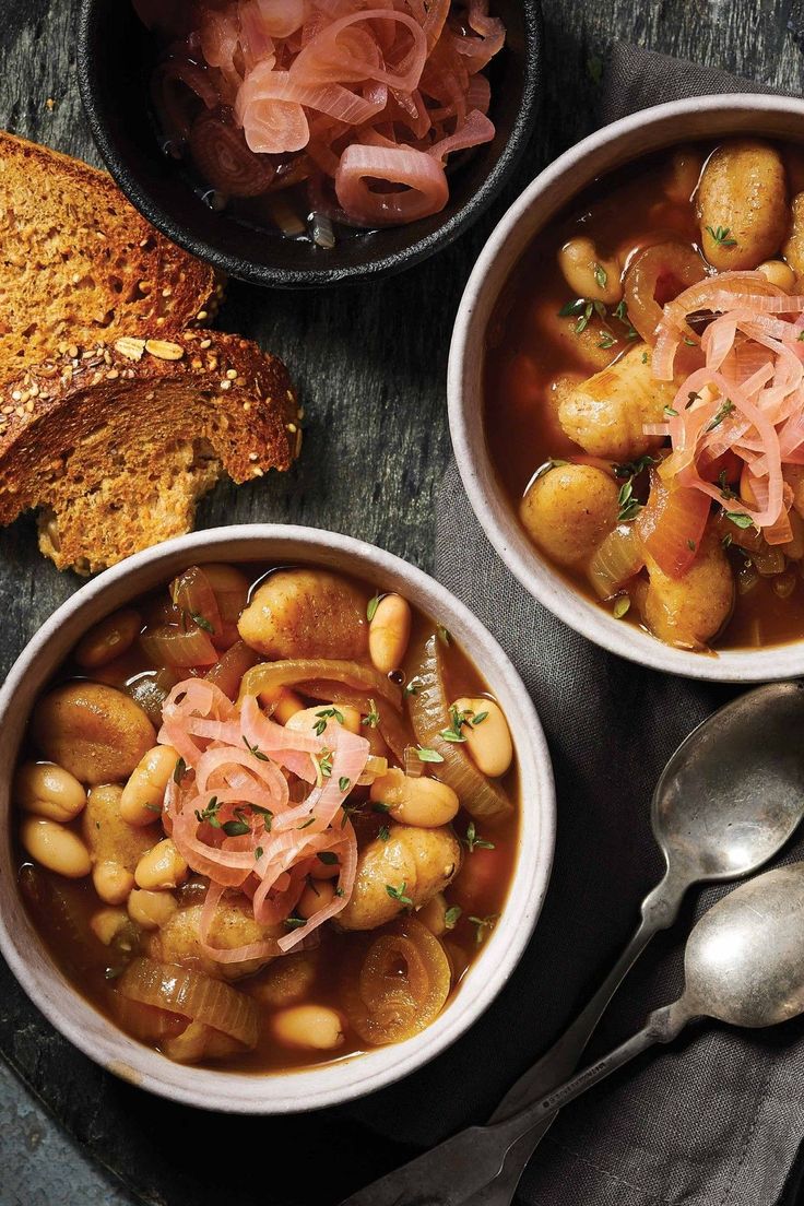 three bowls filled with beans and meat next to bread