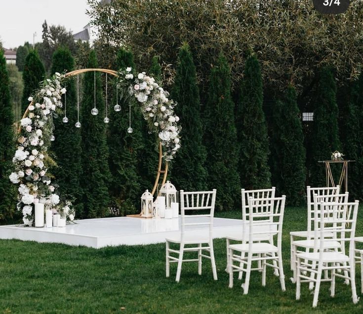 an outdoor wedding setup with white chairs and flowers on the table, surrounded by greenery