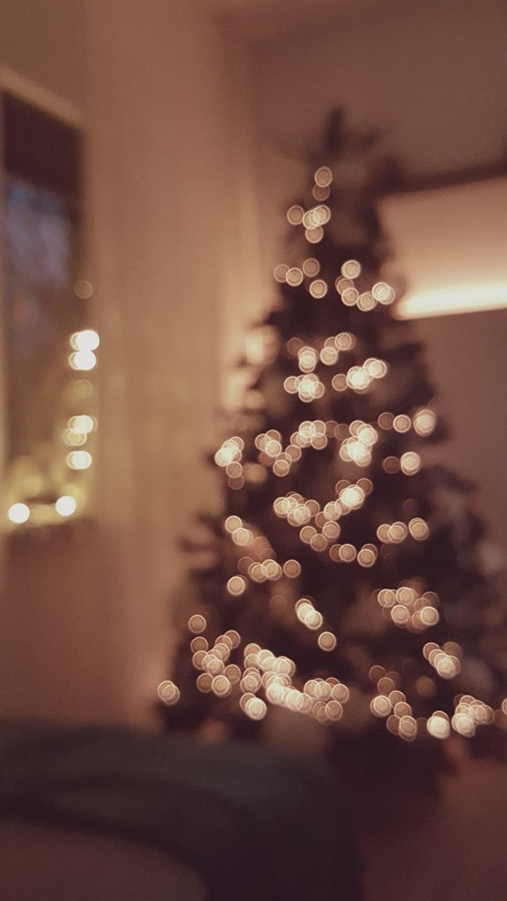 a lit christmas tree in the corner of a room with blurry lights on it