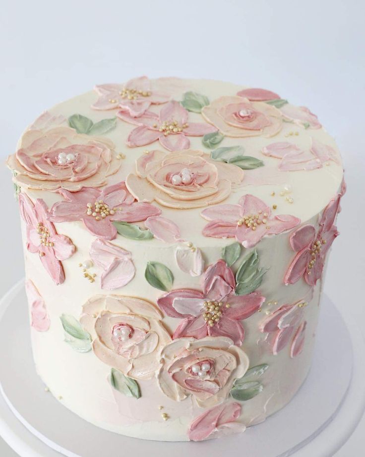 a white cake decorated with pink flowers and green leaves on a plate in front of a white background