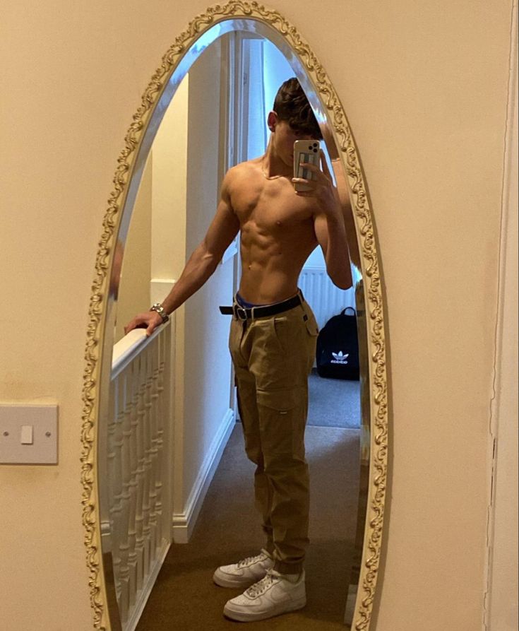 a shirtless man taking a selfie in front of a mirror with his cell phone