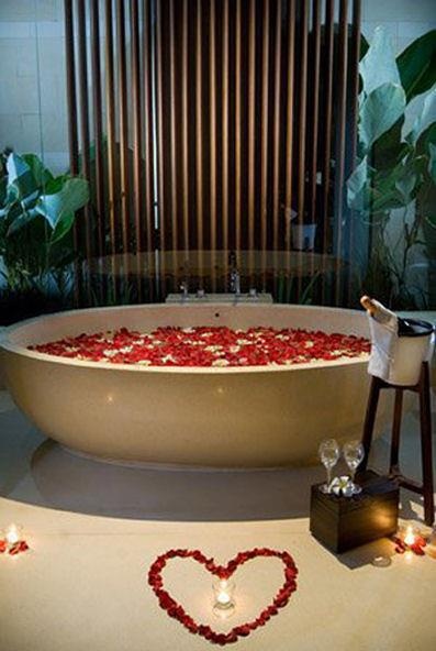 a bathtub filled with rose petals and candles next to a heart - shaped candle holder