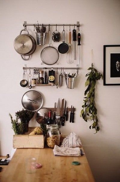 pots and pans are hanging on the wall above a kitchen counter with utensils