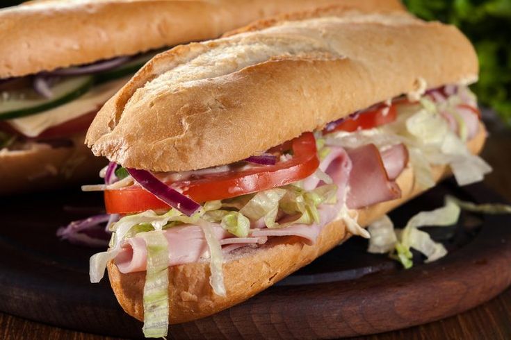 two sub sandwiches with meat, lettuce and tomato on a wooden platter