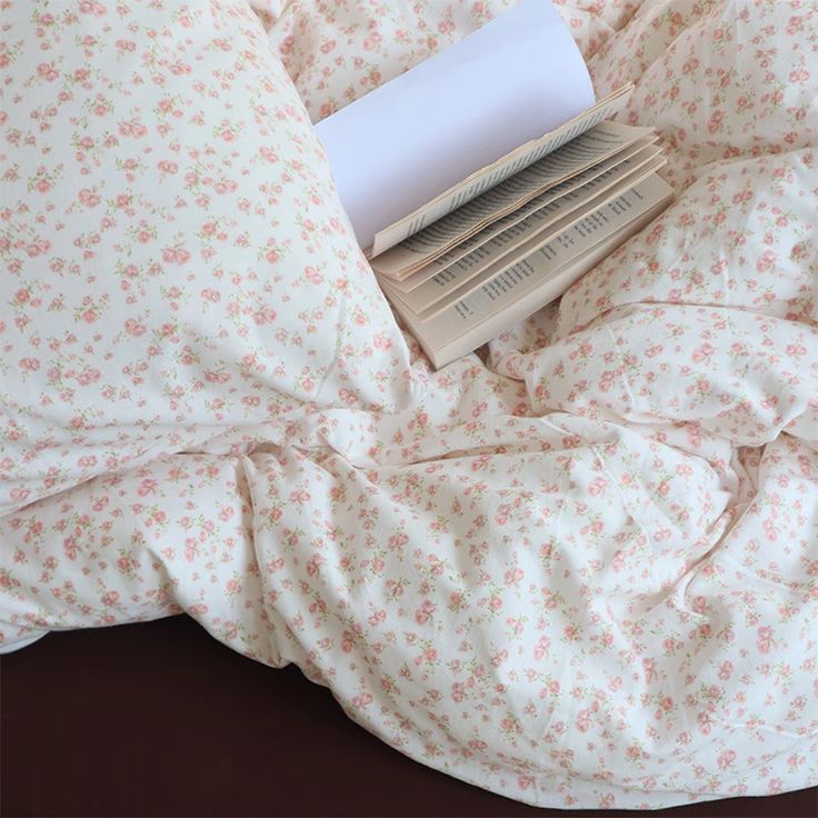 a stack of books sitting on top of a bed covered in white and pink flowers