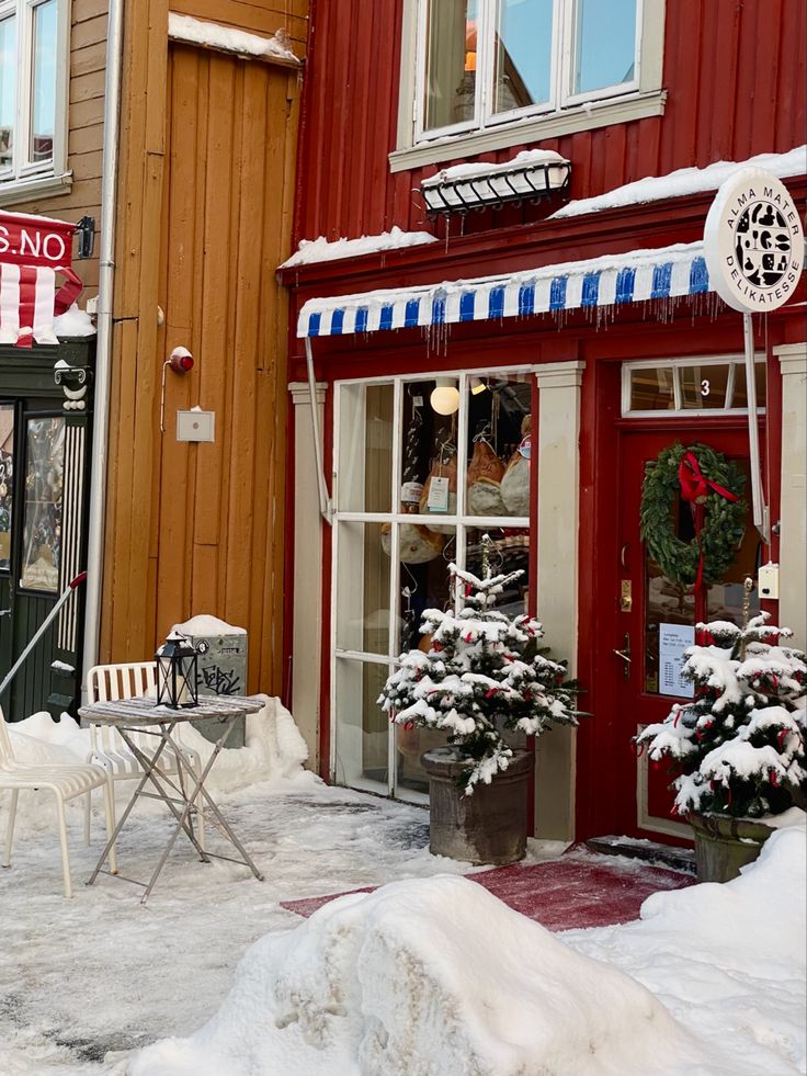 a red building with snow on the ground and two chairs outside in front of it