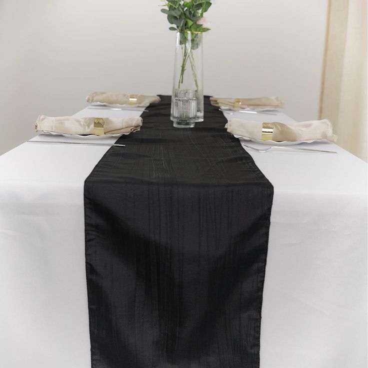 the table is set with black linens and silverware, along with a vase filled with flowers