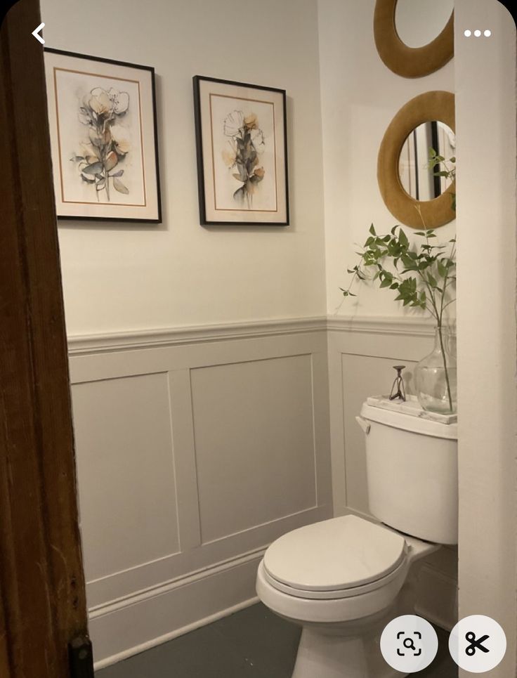 a white toilet sitting next to a sink in a bathroom under two framed pictures on the wall