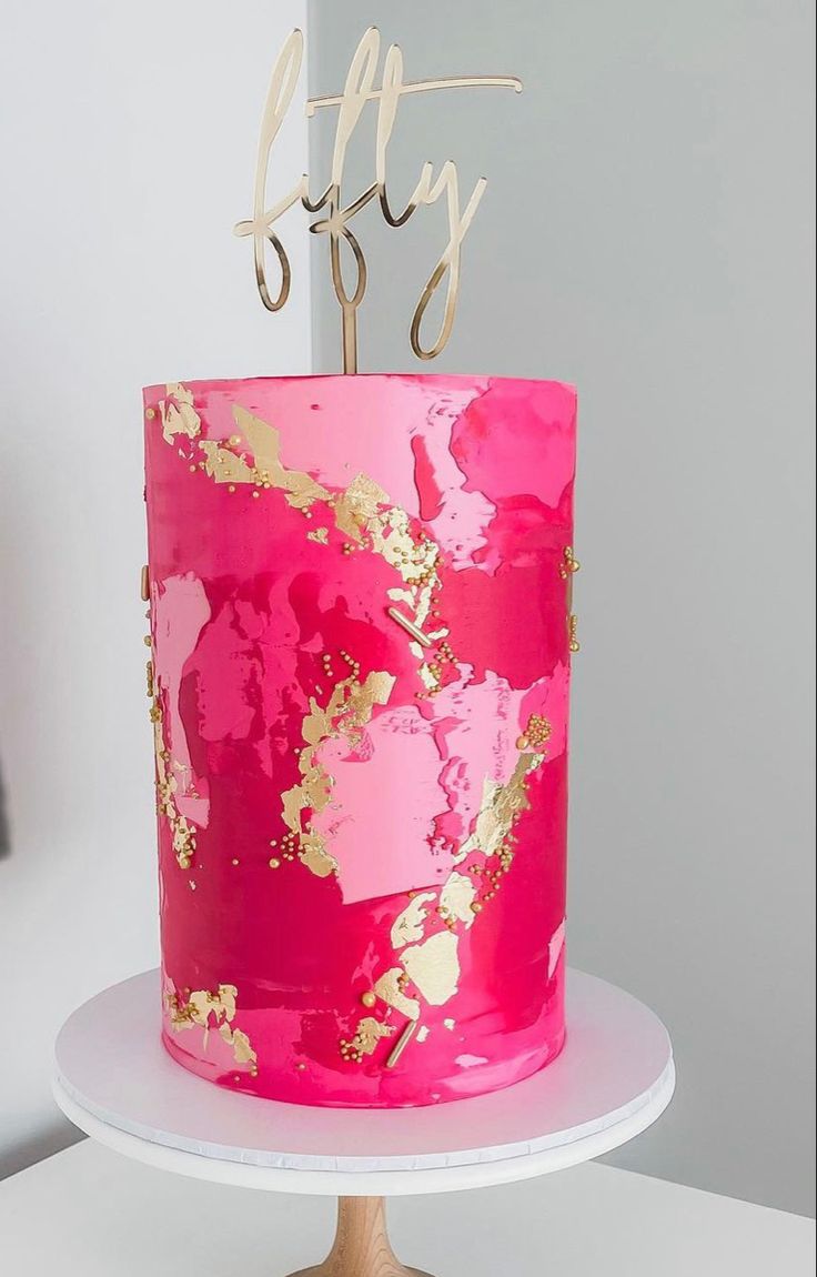 a pink and gold cake with the word fifty on top