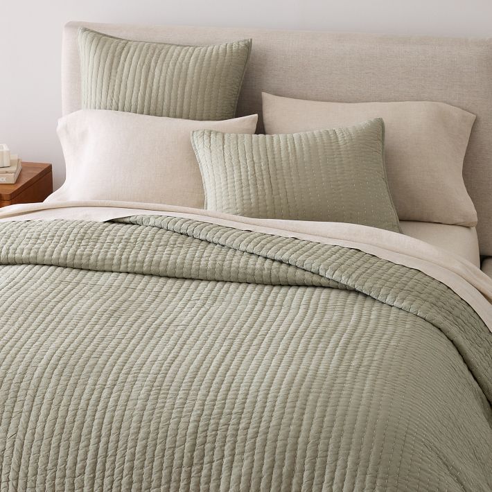 a bed with green bedspread and pillows on top of the headboard, next to a night stand