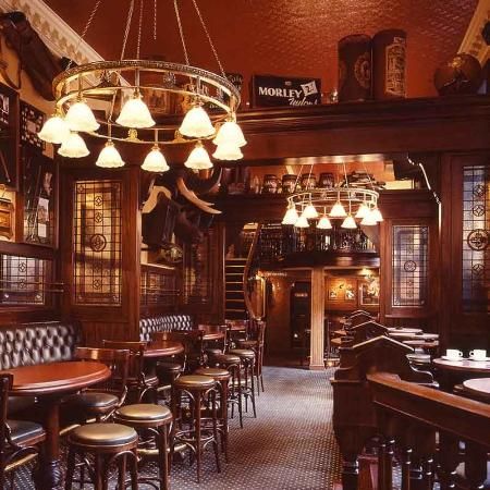 the interior of a bar with many tables and stools, lights hanging from the ceiling