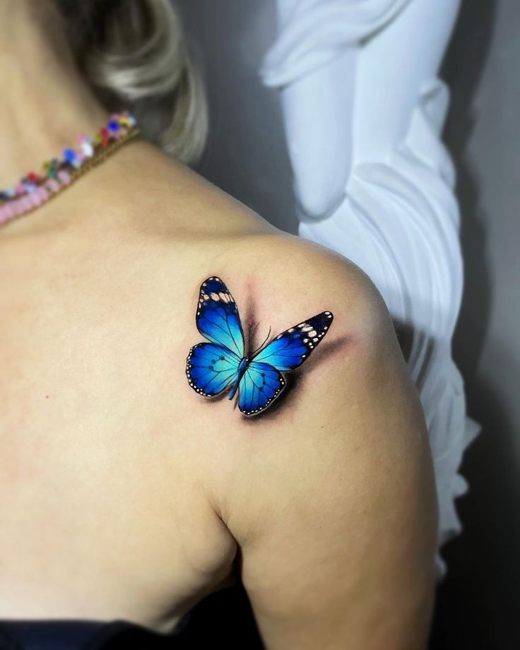 a beautiful blue butterfly tattoo on the back of a woman's left shoulder by peter diamond