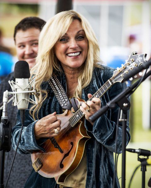 a woman holding a guitar while standing next to a microphone