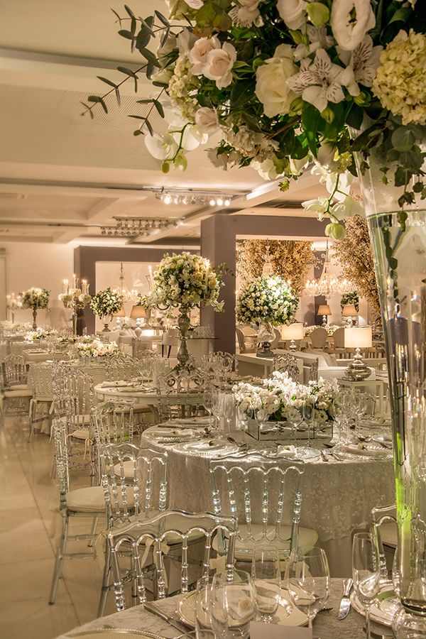 the tables are set up for a formal function with white flowers and greenery in tall vases