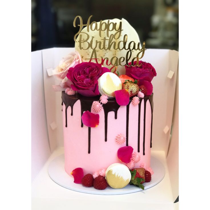 a pink birthday cake with chocolate drips and flowers on top is sitting on a white chair