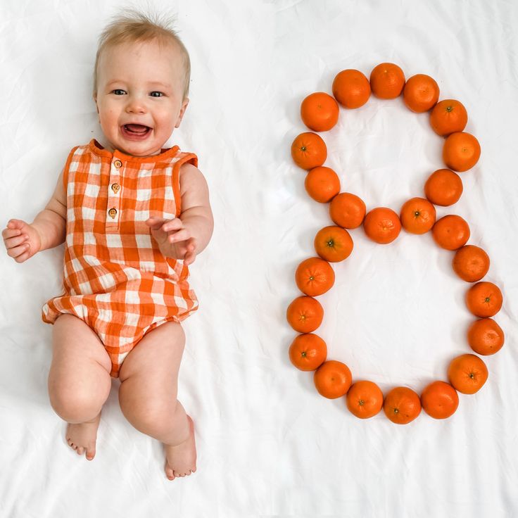 a baby laying next to an orange necklace