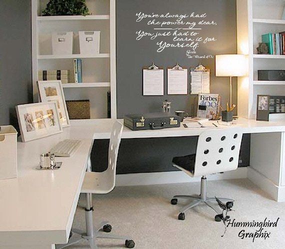 a white desk sitting under a window next to a lamp and bookshelf in a room