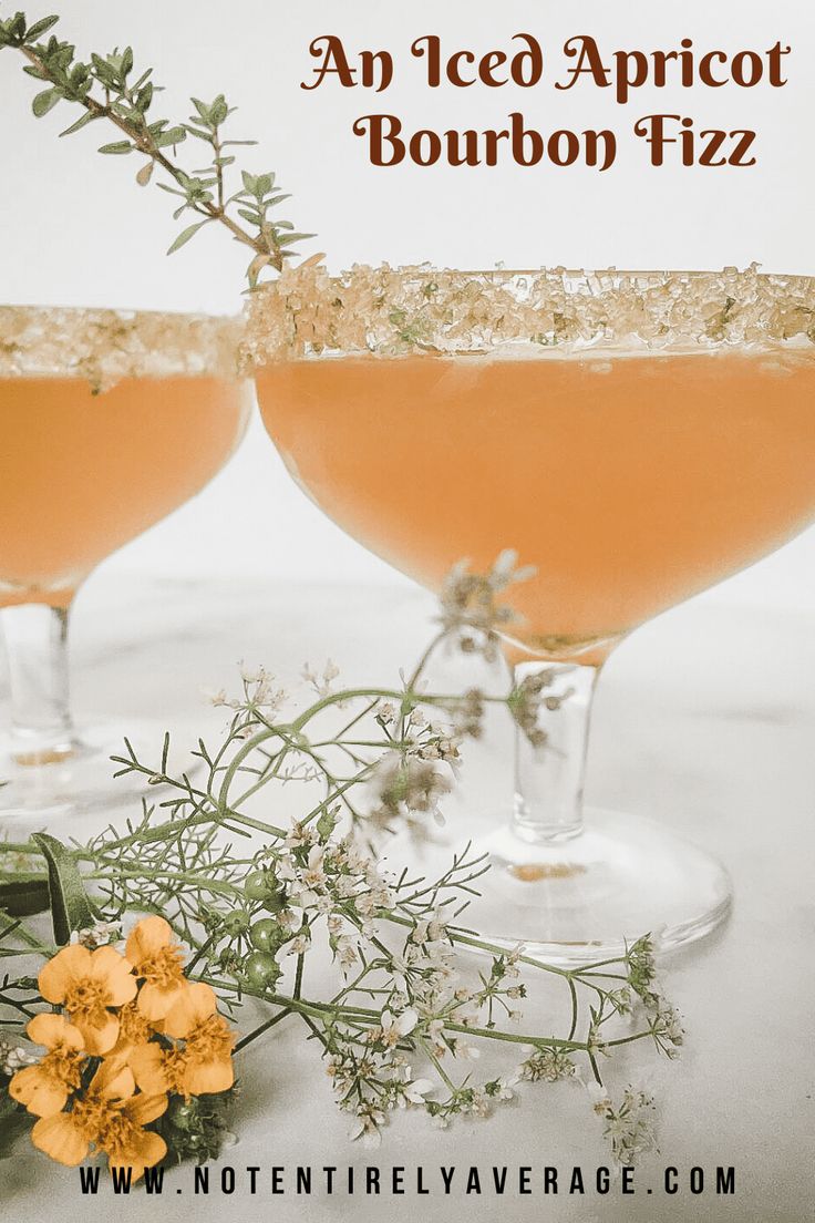 two glasses filled with an iced apricot bourbon fizz next to some flowers