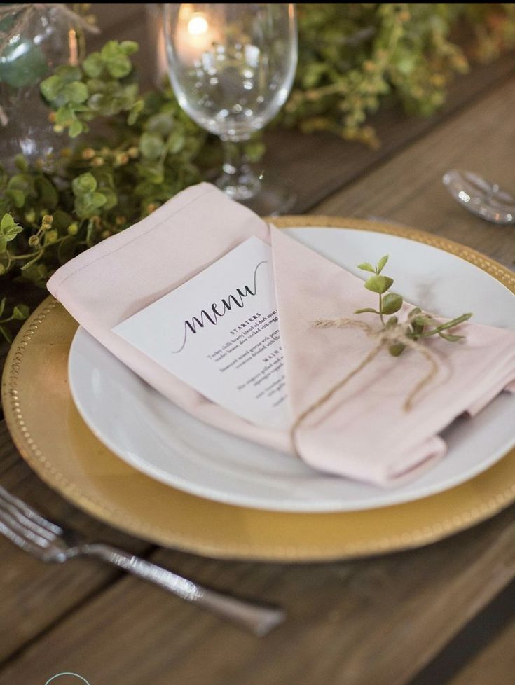 a place setting with pink napkins and greenery