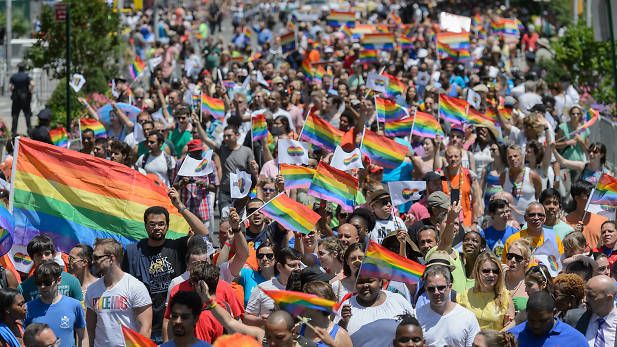 a large group of people walking down a street holding rainbow flags