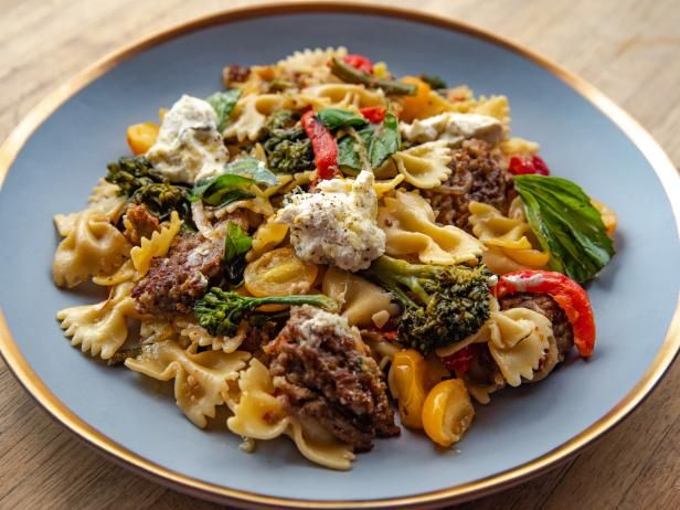 a pasta dish with meat, broccoli and peppers on a blue plate sitting on a wooden table